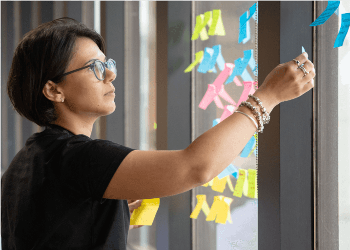 A person placing a post-it note on a window with other notes