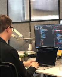 A software engineer at a workstation with a laptop and a wide external monitor
