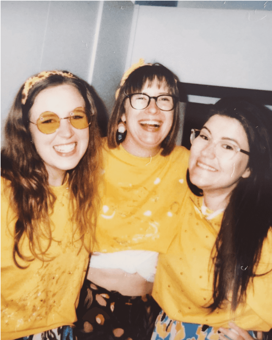 A Polaroid-style image of three staff members dressed up in yellow and laughing