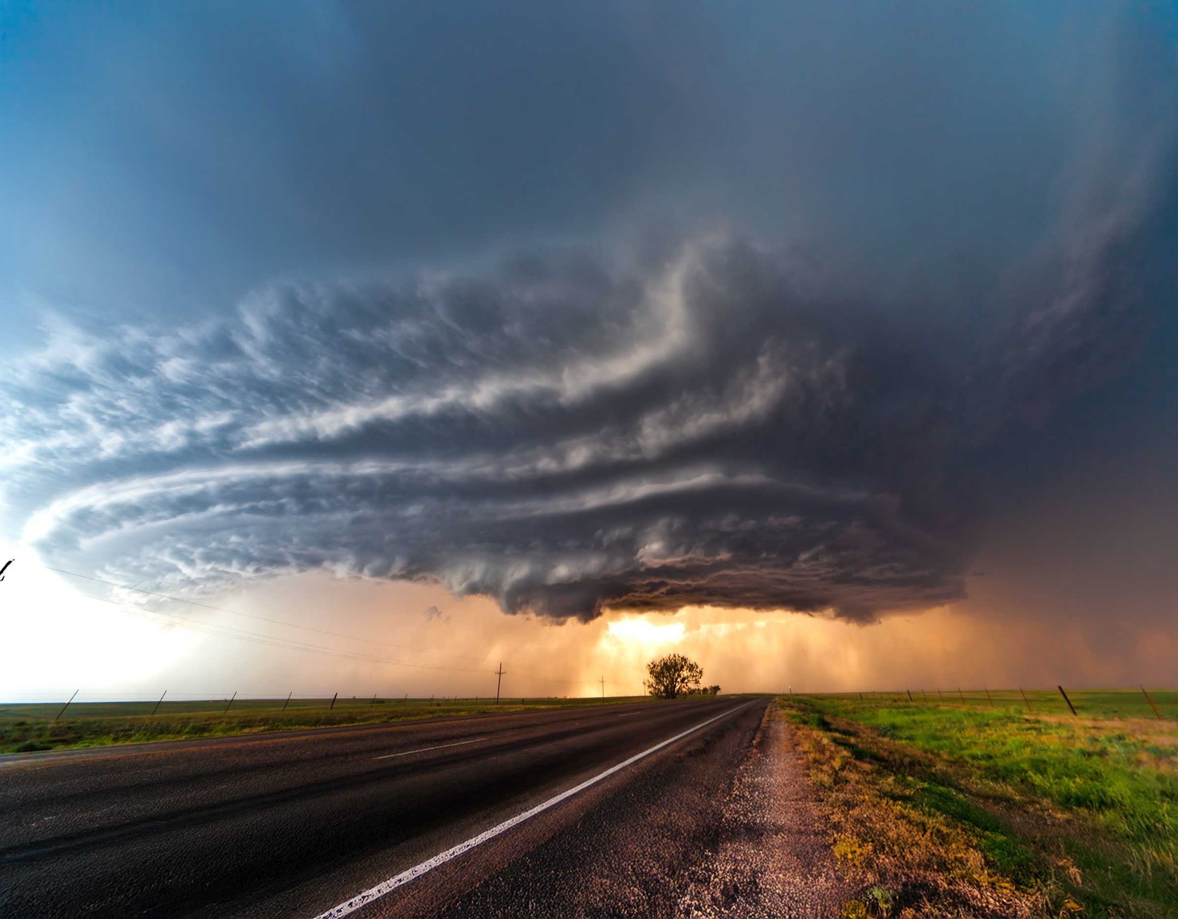 A dramatic supercell storm cloud over a flat landscape with a road stretching toward the horizon.