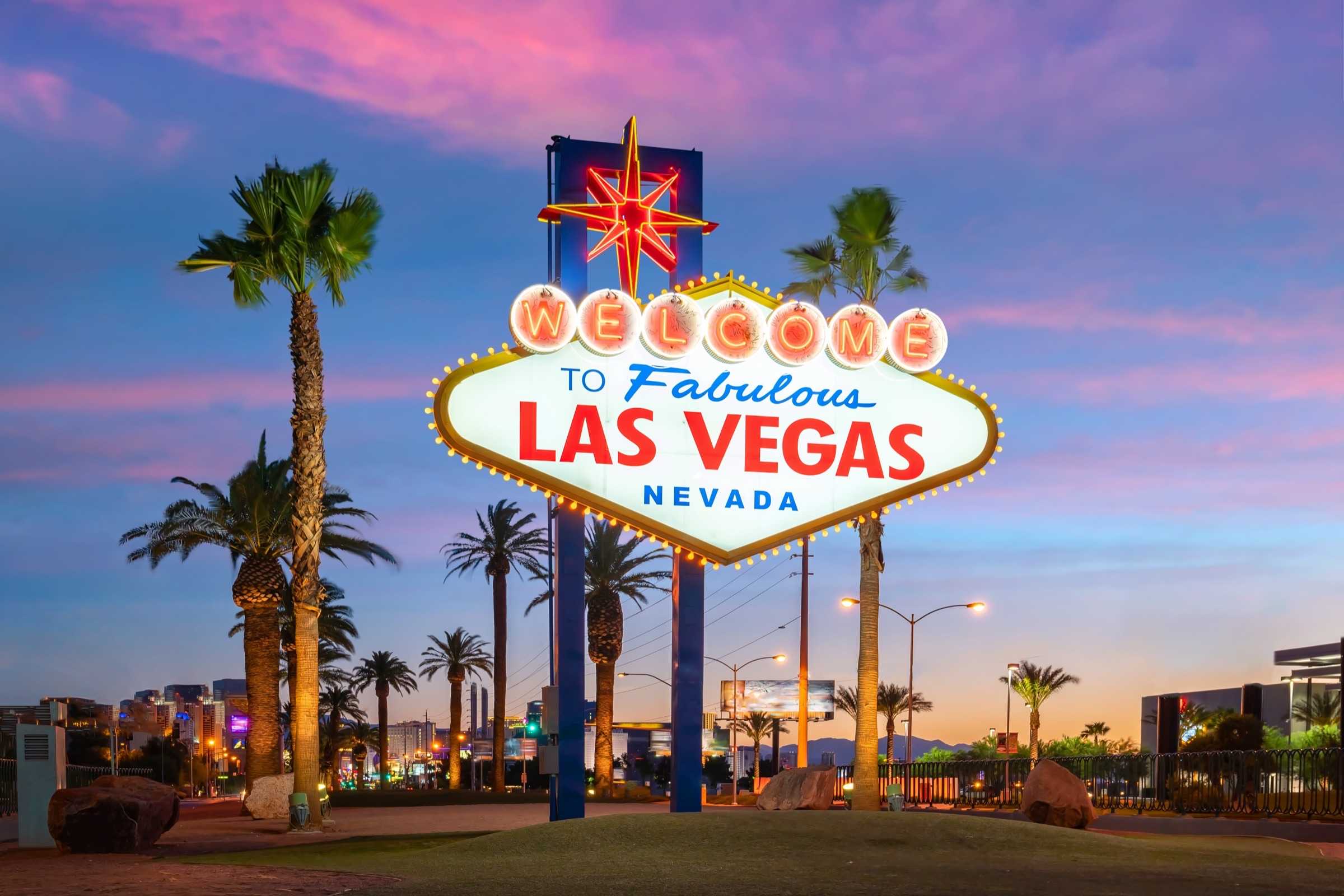 The Welcome to Fabulous Las Vegas sign lit up at dusk, surrounded by palm trees.