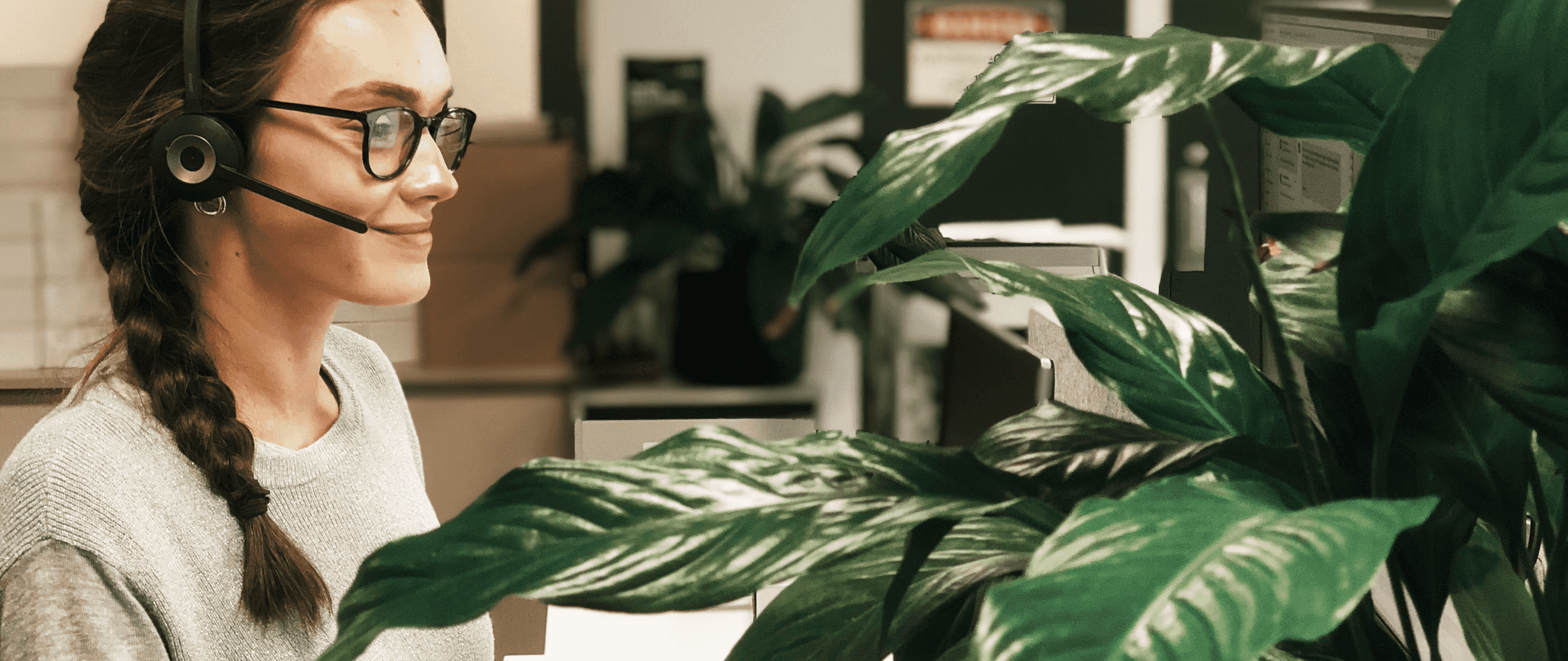 A receptionist sits at a desk adorned with green tropical plants