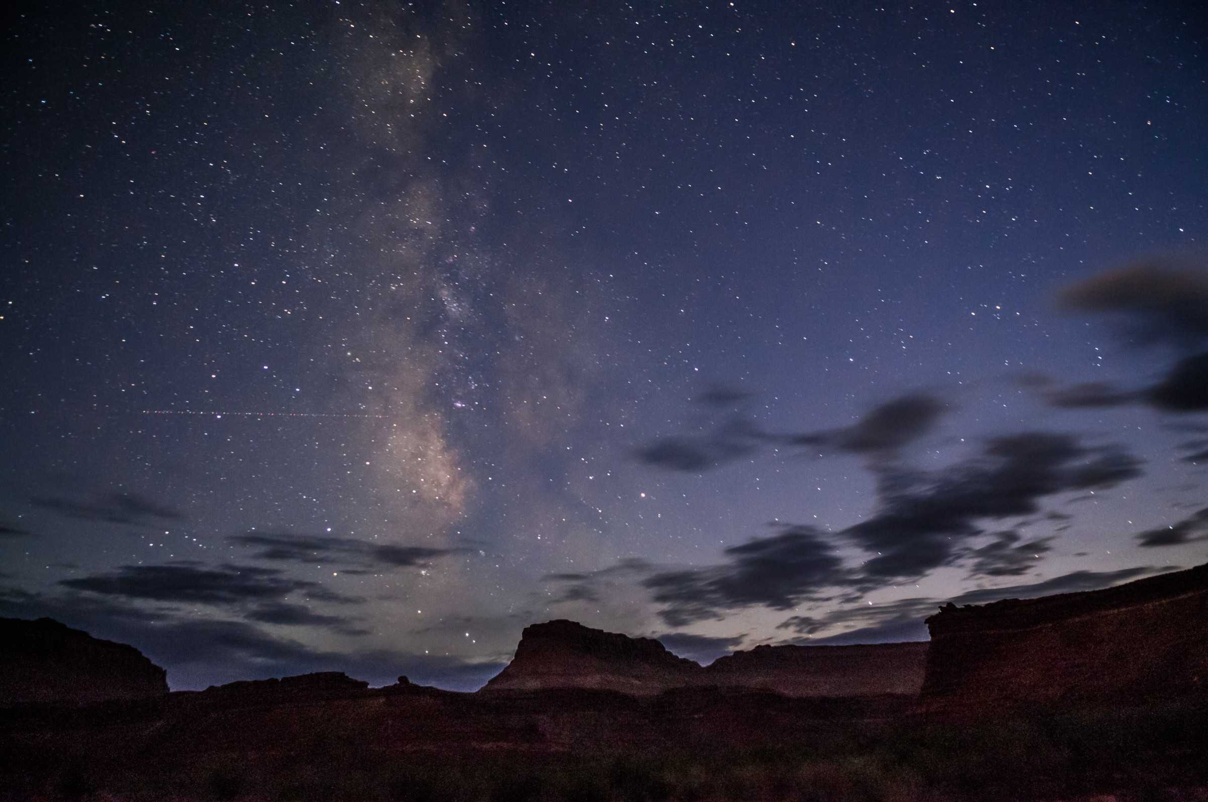 The Milky Way over a dark desert landscape with mesas.