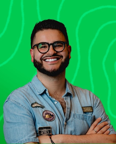 A Stile Teaching and Learning Specialist smiling with arms crossed, in front of a green background with abstract line patterns.