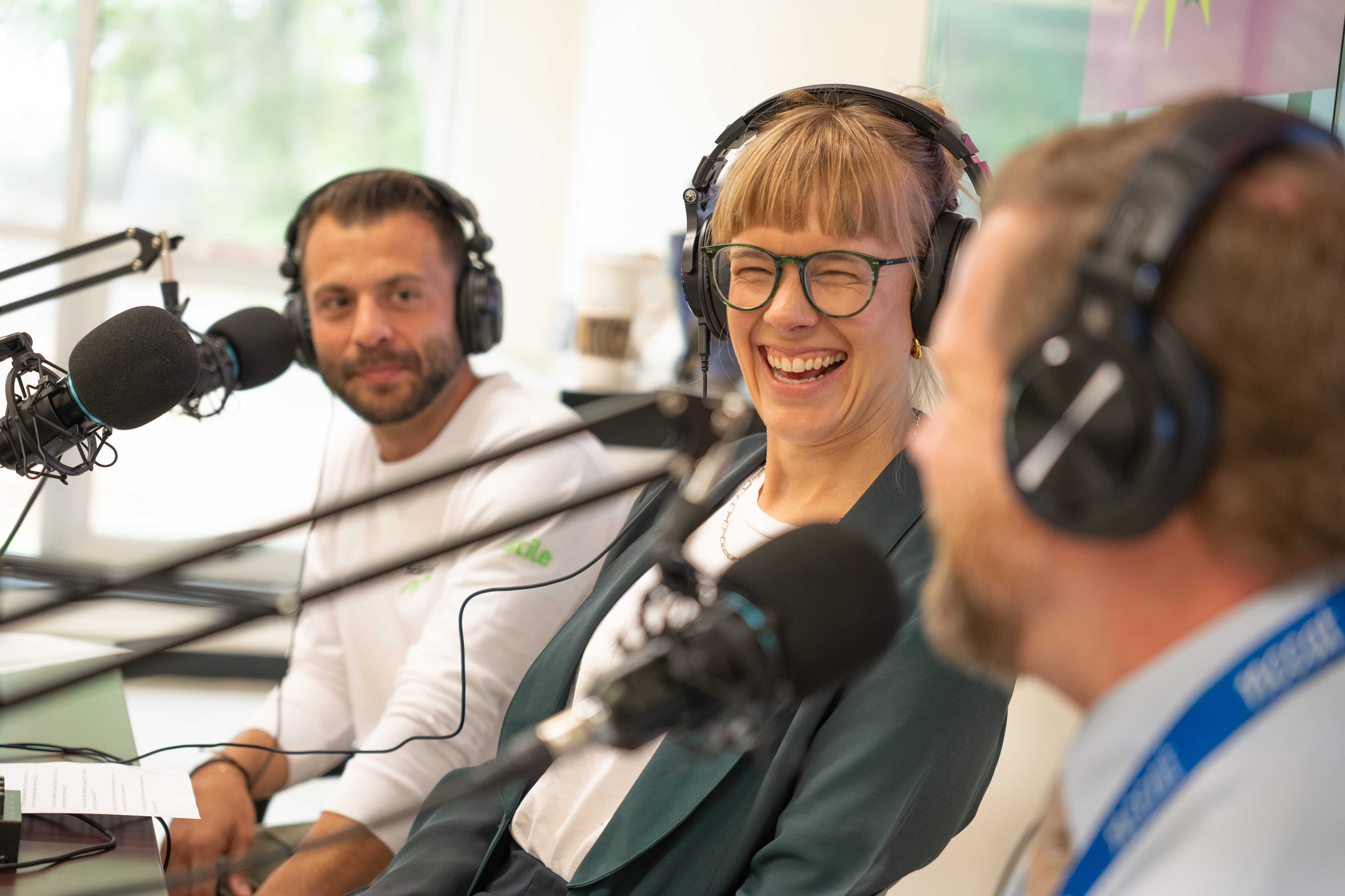 Three people recording a podcast. The centre person is smiling and laughing.