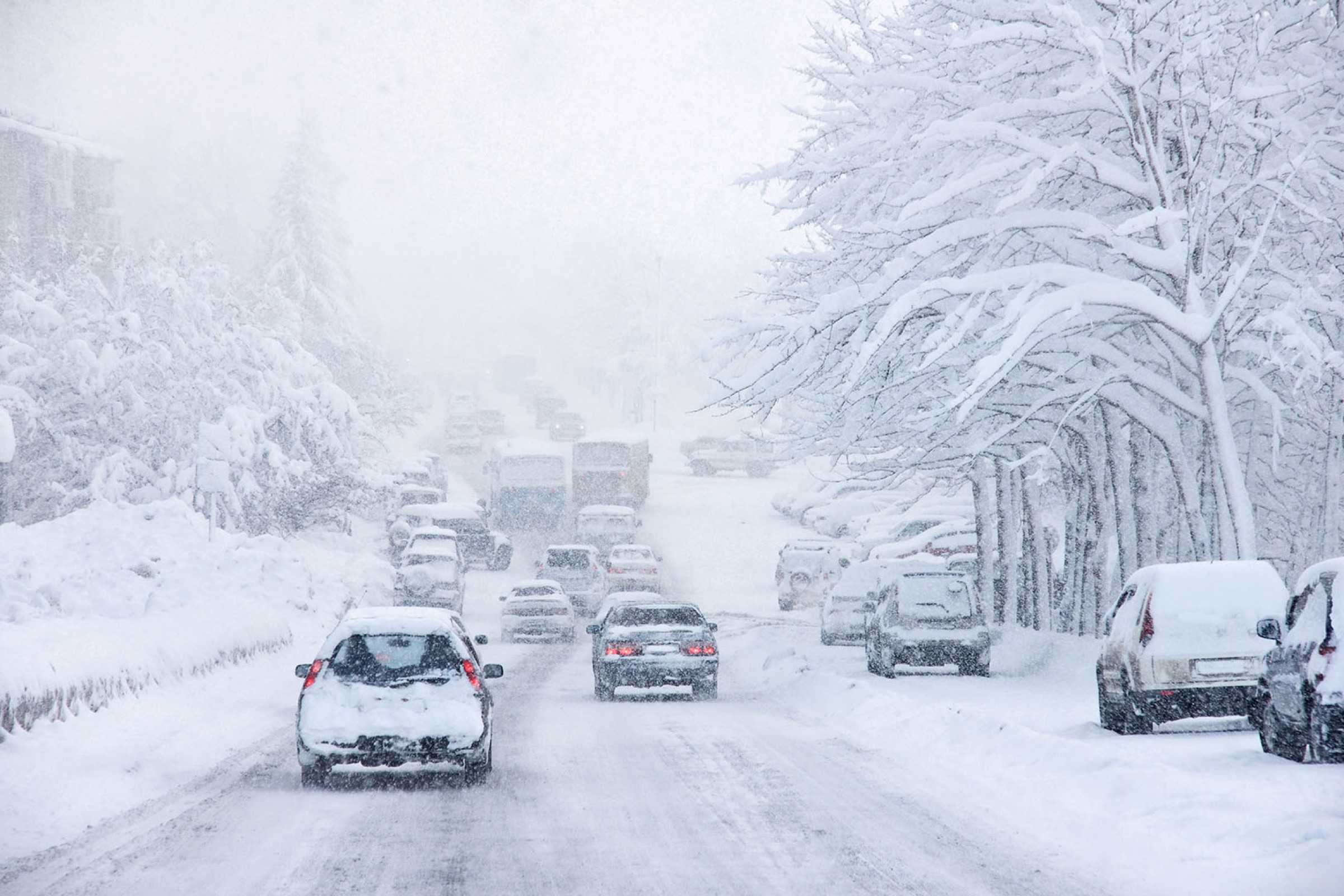 Cars driving through heavy lake-effect snow on a highway during a winter storm.