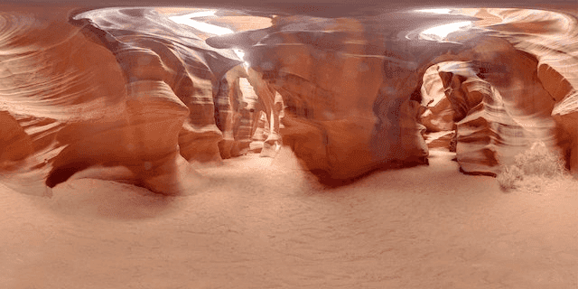 Red rock formations with sandy ground around it, distorted like looking through a curved lense