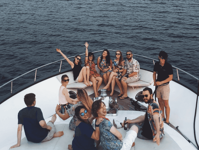 A group of people smiling and positing on the tip of a yacht.