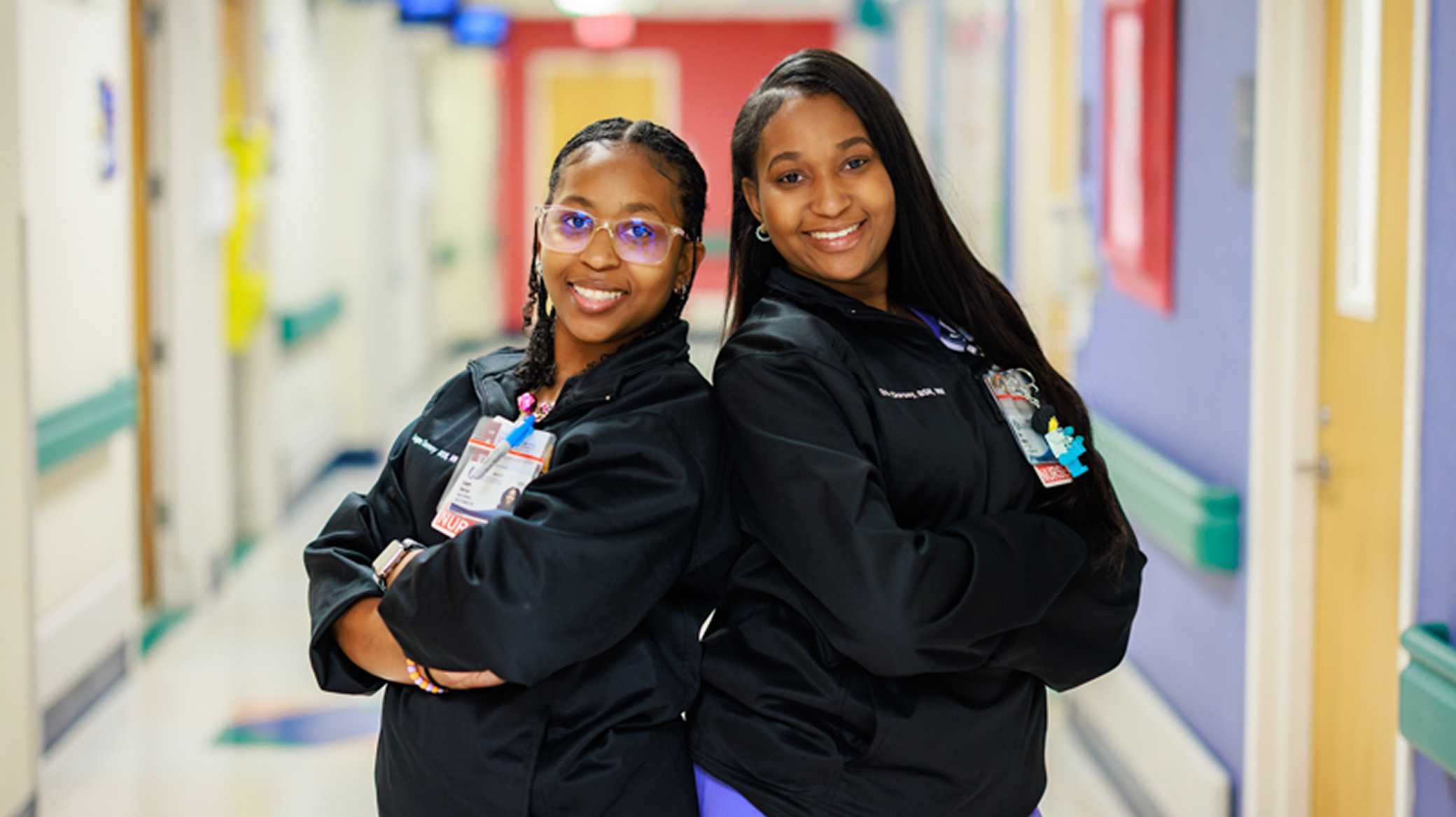 Two nurses in a hospital, smiling and standing back-to-back