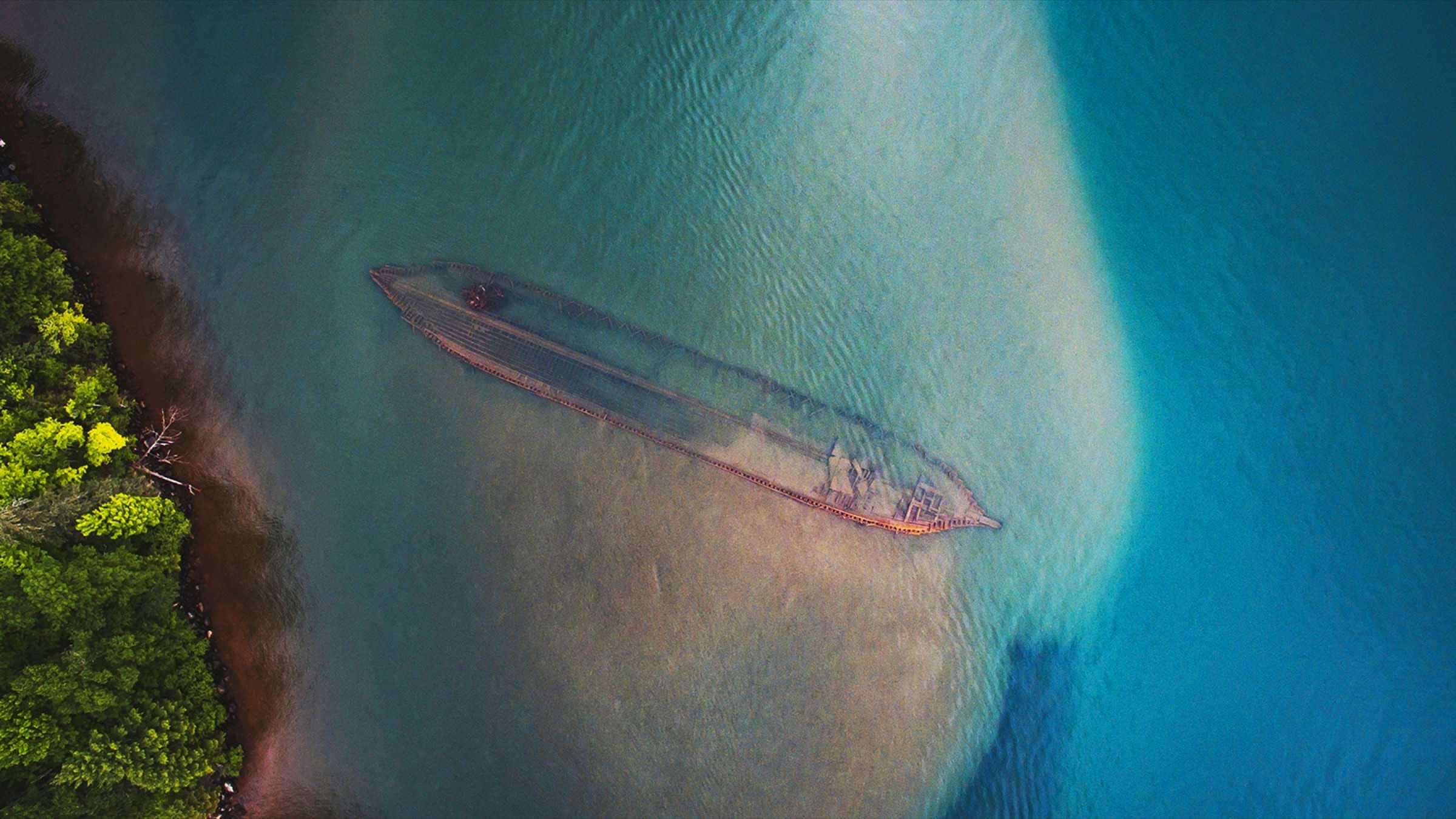 An aerial view of a shipwreck visible through clear turquoise water in the Great Lakes.